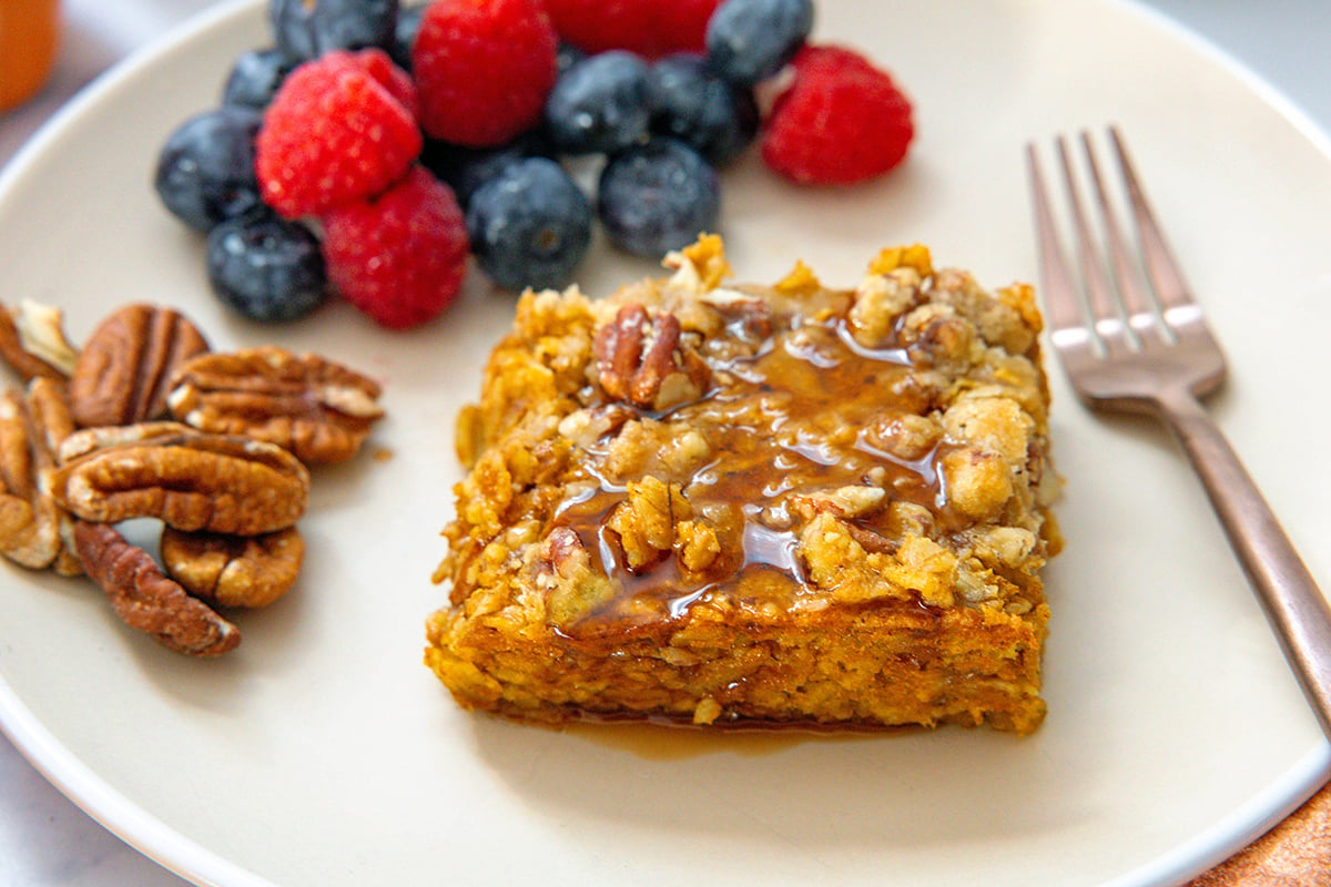 Landscape view of piece of baked pumpkin oatmeal on a plate with fork, berries, and pecans.