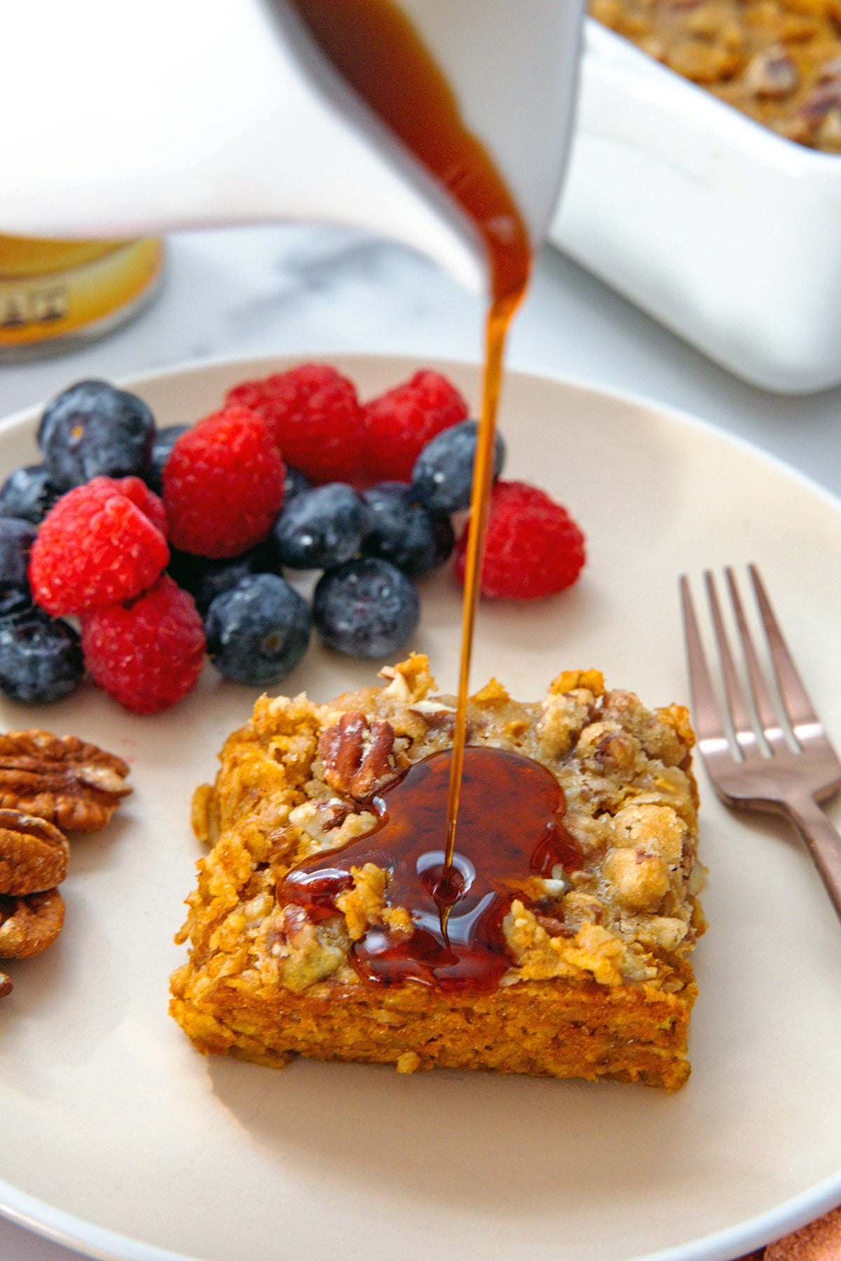 Maple syrup being poured over slice of baked pumpkin oatmeal.