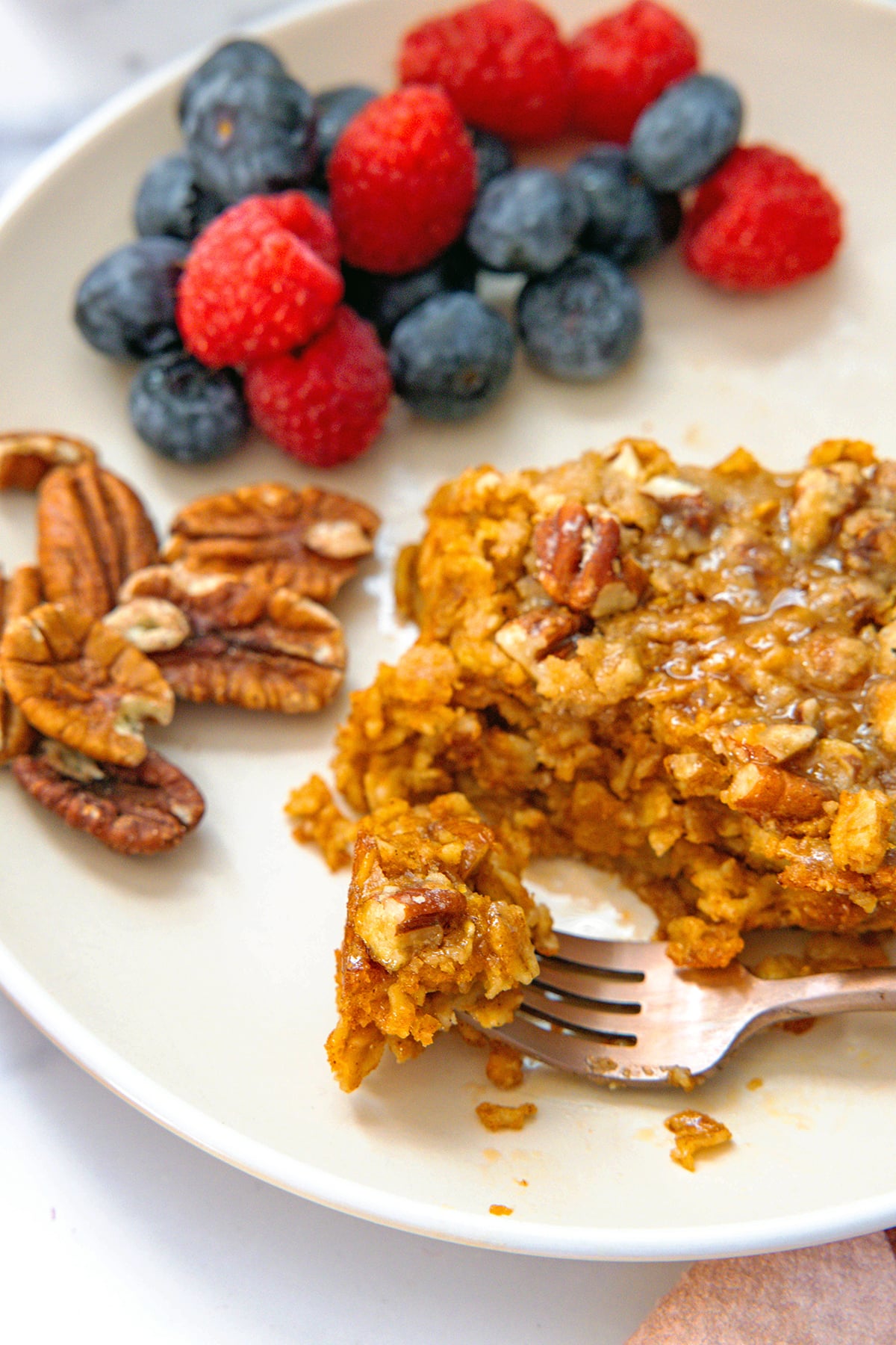 Fork holding piece of baked pumpkin oatmeal on a plate.