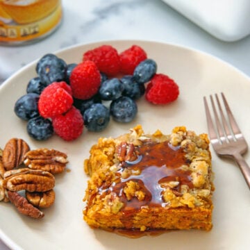 Closeup view of a piece of baked pumpkin oatmeal topped with maple syrup on a plate.