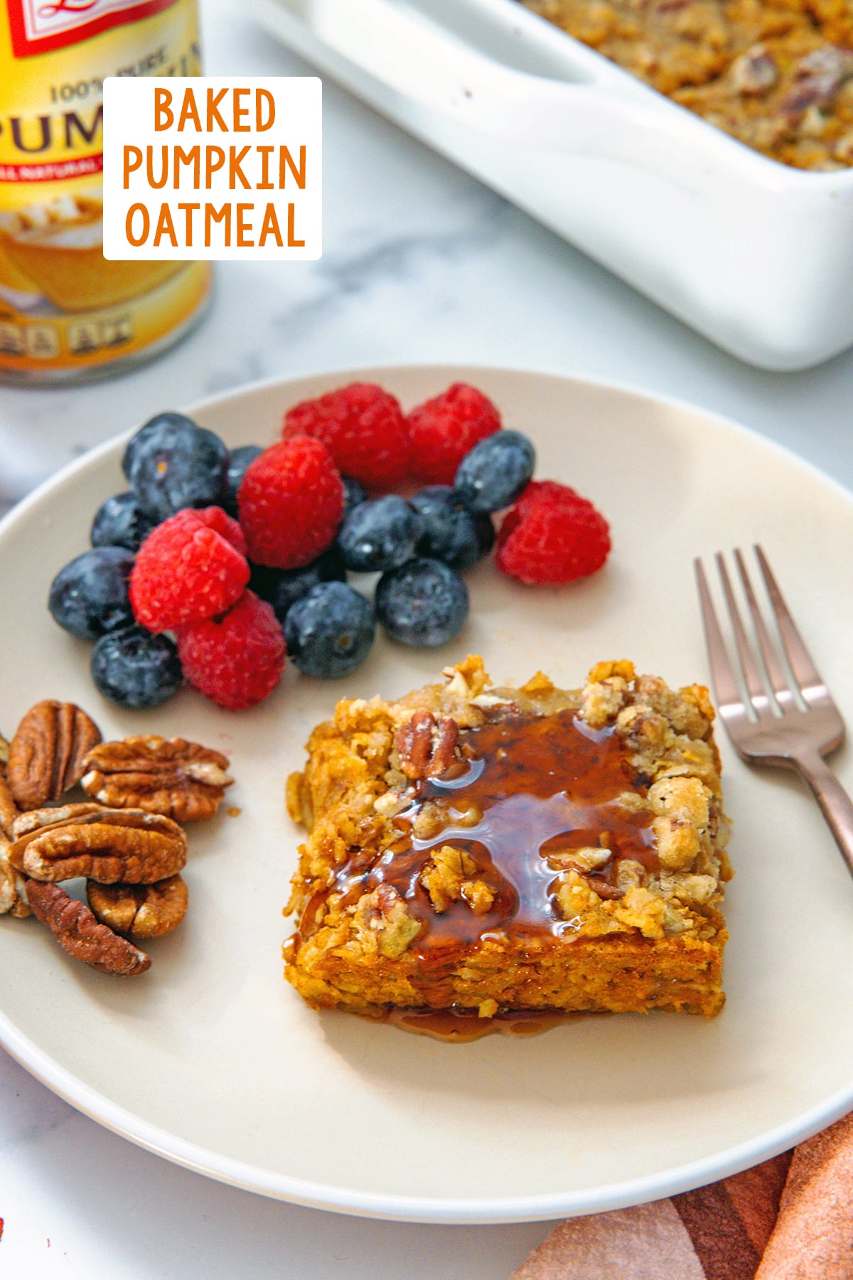 Slice of baked pumpkin oatmeal on a plate with maple syrup and berries and pecans on the side with recipe title at top.
