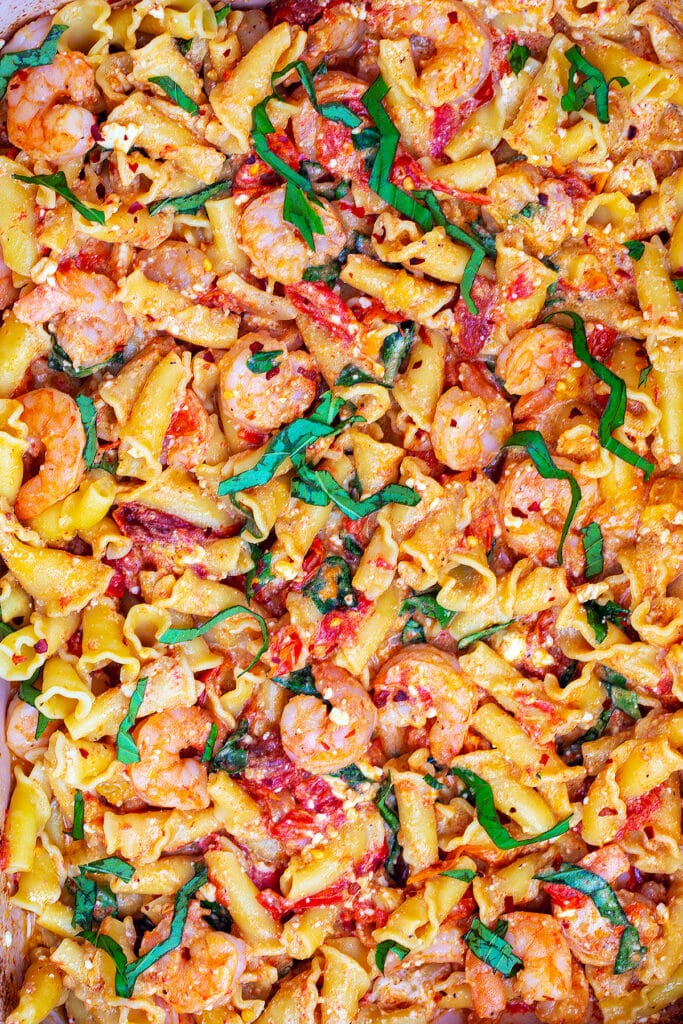 Close-up view of cooked pasta, shrimp, tomatoes, and feta with basil.