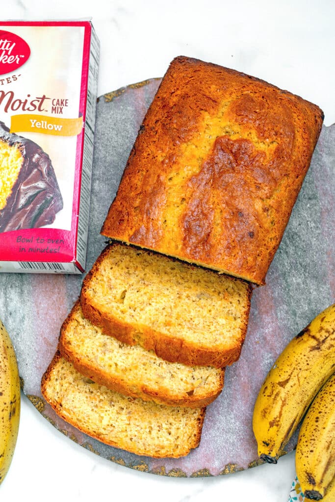 Banana bread with slices cut on pink marble board with box of cake mix.