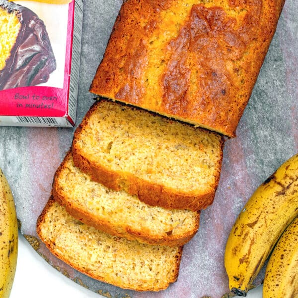 Closeup view of sliced banana bread with pancake mix with box of mix and ripe bananas on side.