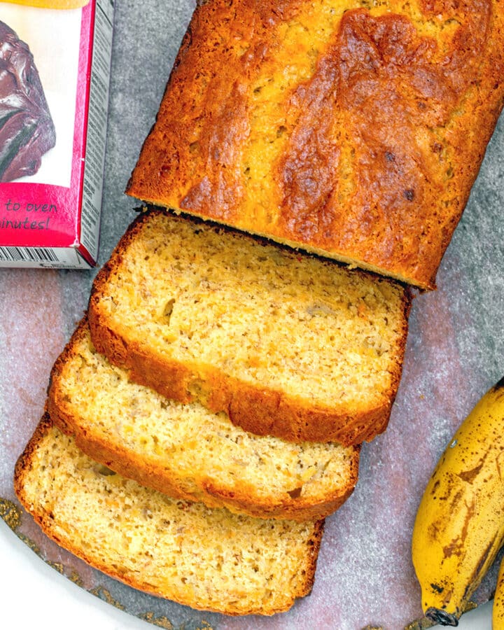 Closeup view of sliced banana bread with pancake mix with box of mix and ripe bananas on side.