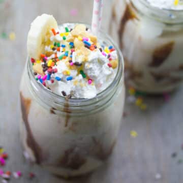 Closeup overhead view of a banana split vodka milkshake topped with whipped cream and rainbow sprinkles.