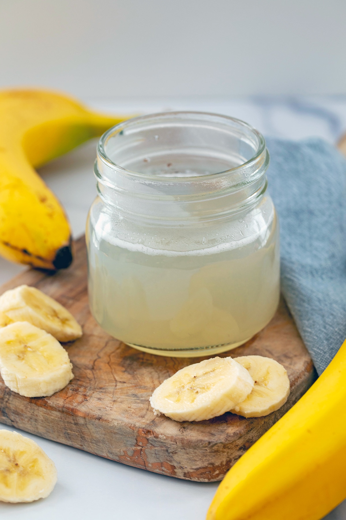 Overhead view of a small mason jar of banana simple syrup with whole and sliced bananas all around.