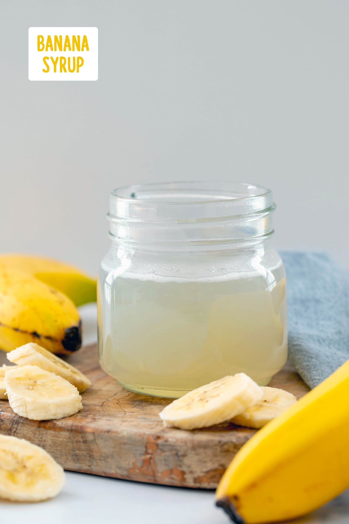 Head-on view of a small jar of banana syrup with whole and sliced bananas all around and recipe title at top.