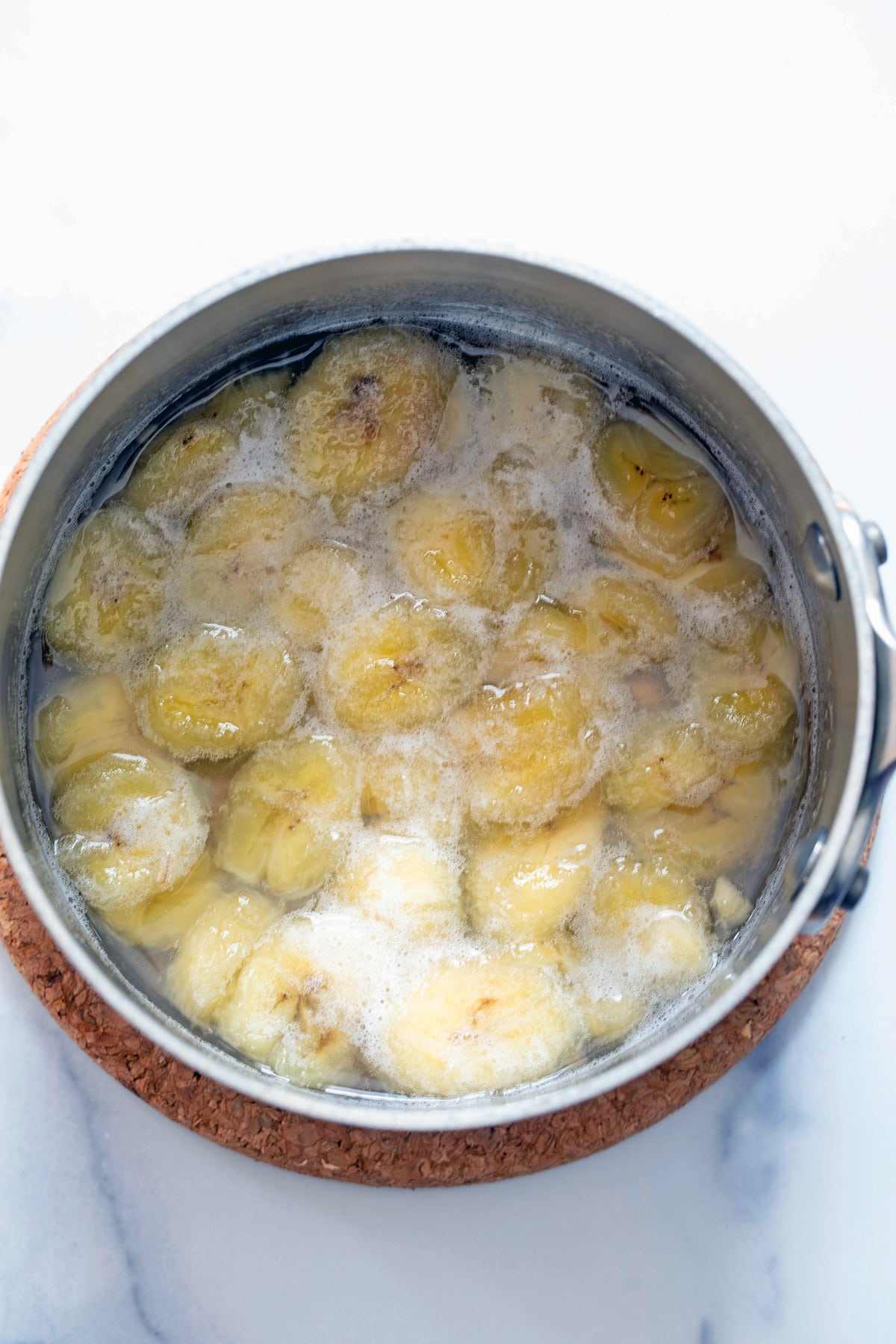 Sliced bananas simmering in sugar water in saucepan.