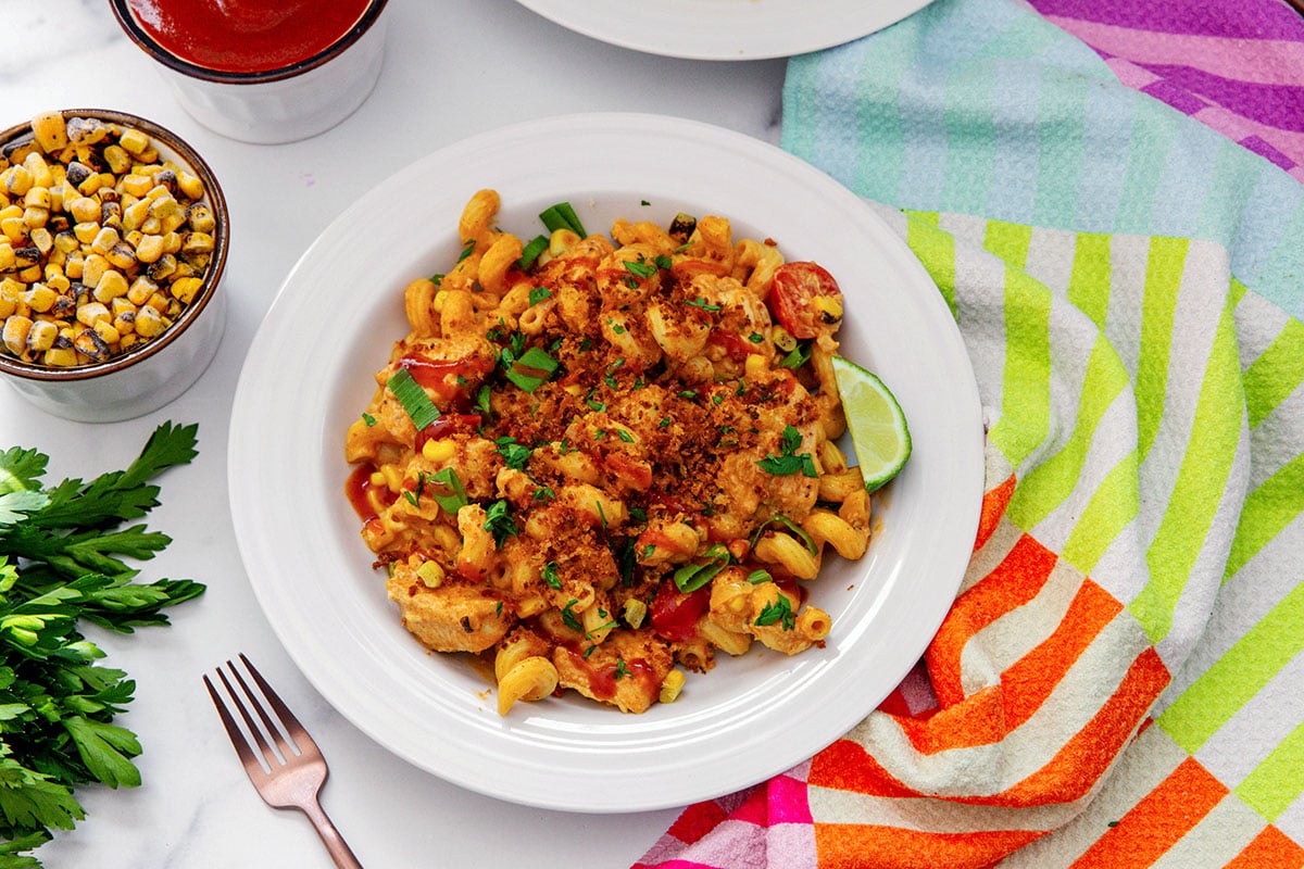 Landscape overhead view of a plate of BBQ chicken pasta with parsley, fork, and corn on the side.
