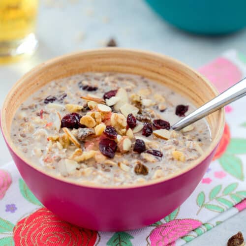 Closeup view of a bowl of bircher muesli with nuts and dried fruit on top.