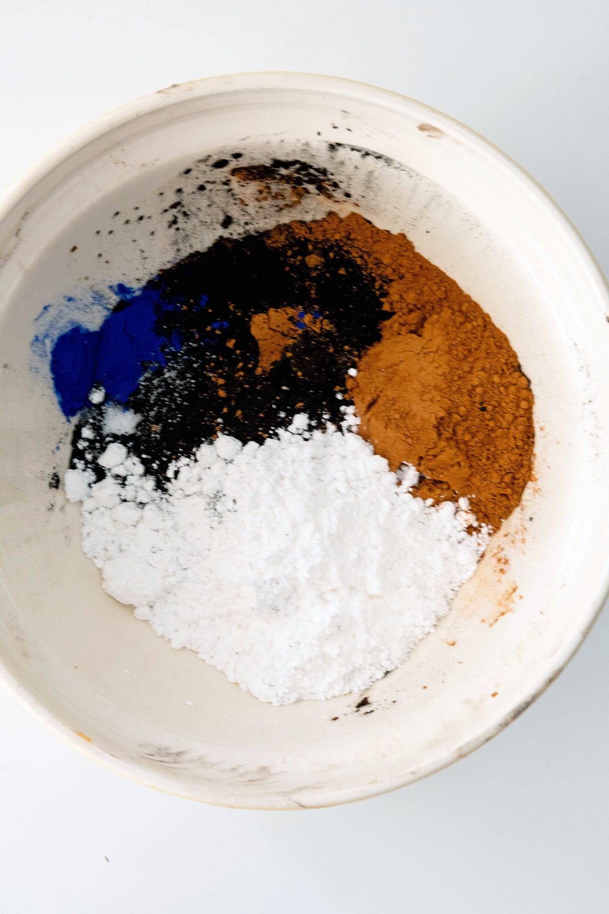 Ingredients for chocolate cake powder in bowl, including confectioners' sugar, black coco powder, regular cocoa powder, and blue spirulina powder.