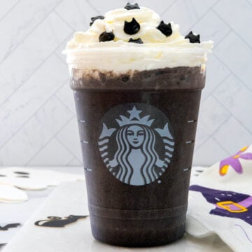 Closeup view of a Black Cat Frappuccino with whipped cream and sprinkles in Starbucks cup.