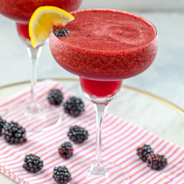 Closeup view of a blackberry lemonade margarita with lemon garnish and blackberries all around.