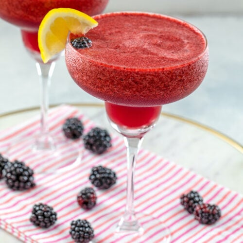 Closeup view of a blackberry lemonade margarita with lemon garnish and blackberries all around.