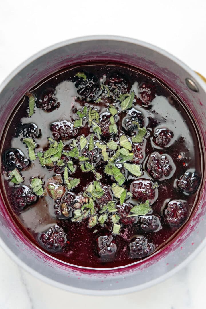 Blackberry syrup in a saucepan with chopped sage over it.