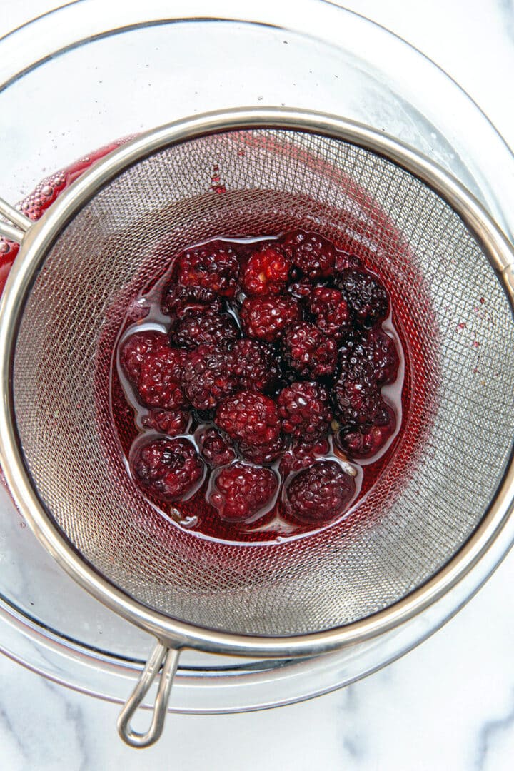 blackberries and sage being strained out of syrup.