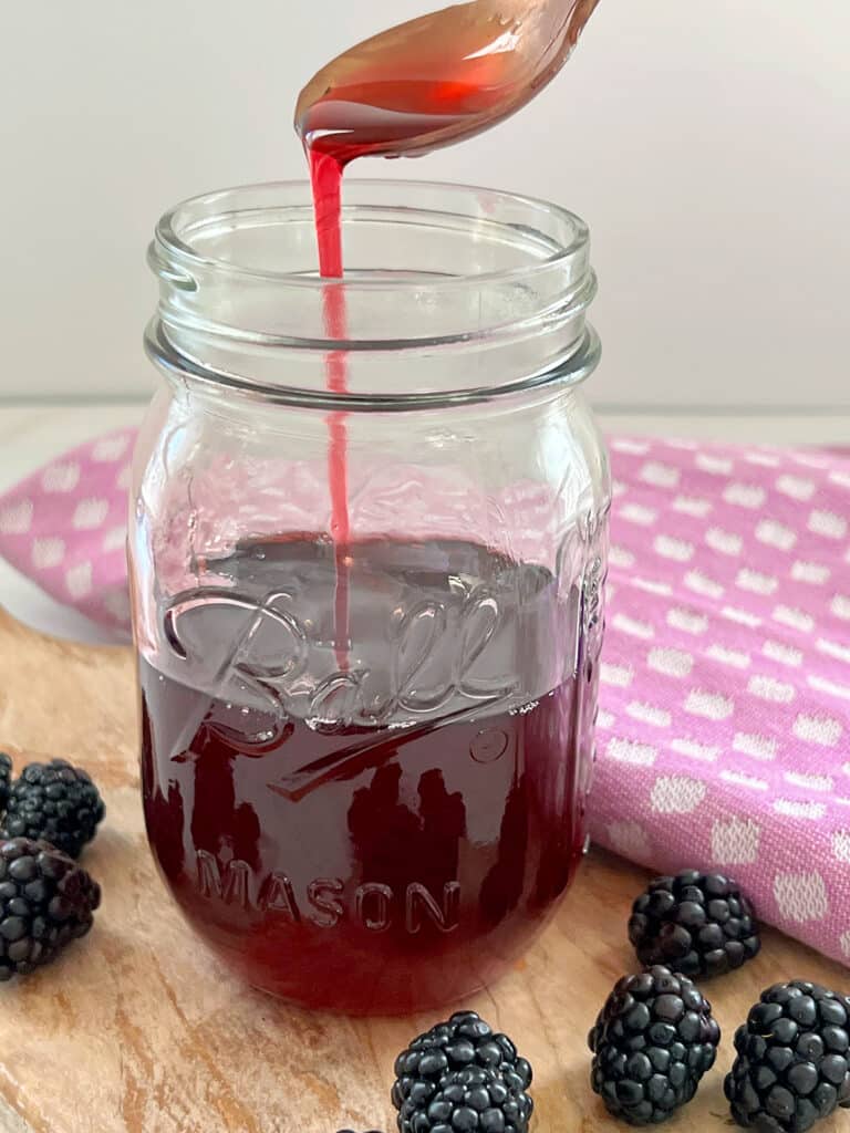 Blackberry syrup dripping off spoon into jar.