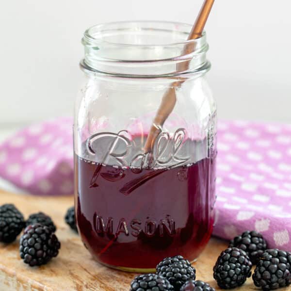 Closeup view of jar of blackberry simple syrup with fresh blackberries.