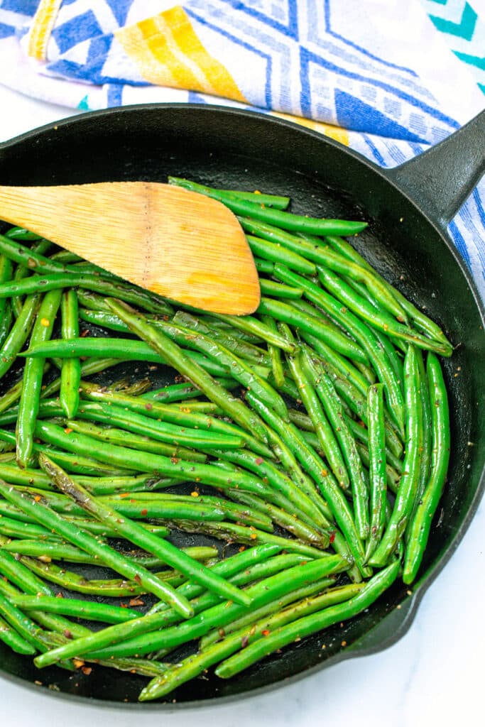 Blistered green beans in a cast iron skillet with wooden spatula.