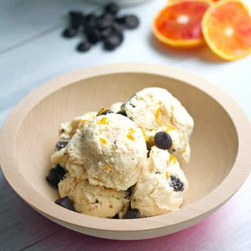 Closeup view of a bowl of blood orange ice cream with dark chocolate chips.