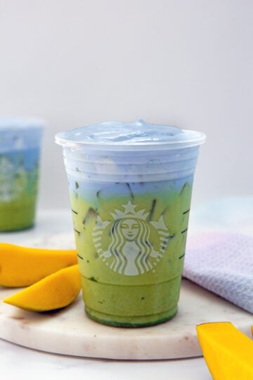 Head-on view of an iced Blue Coconut Matcha in a Starbucks cup with sliced mango all around.