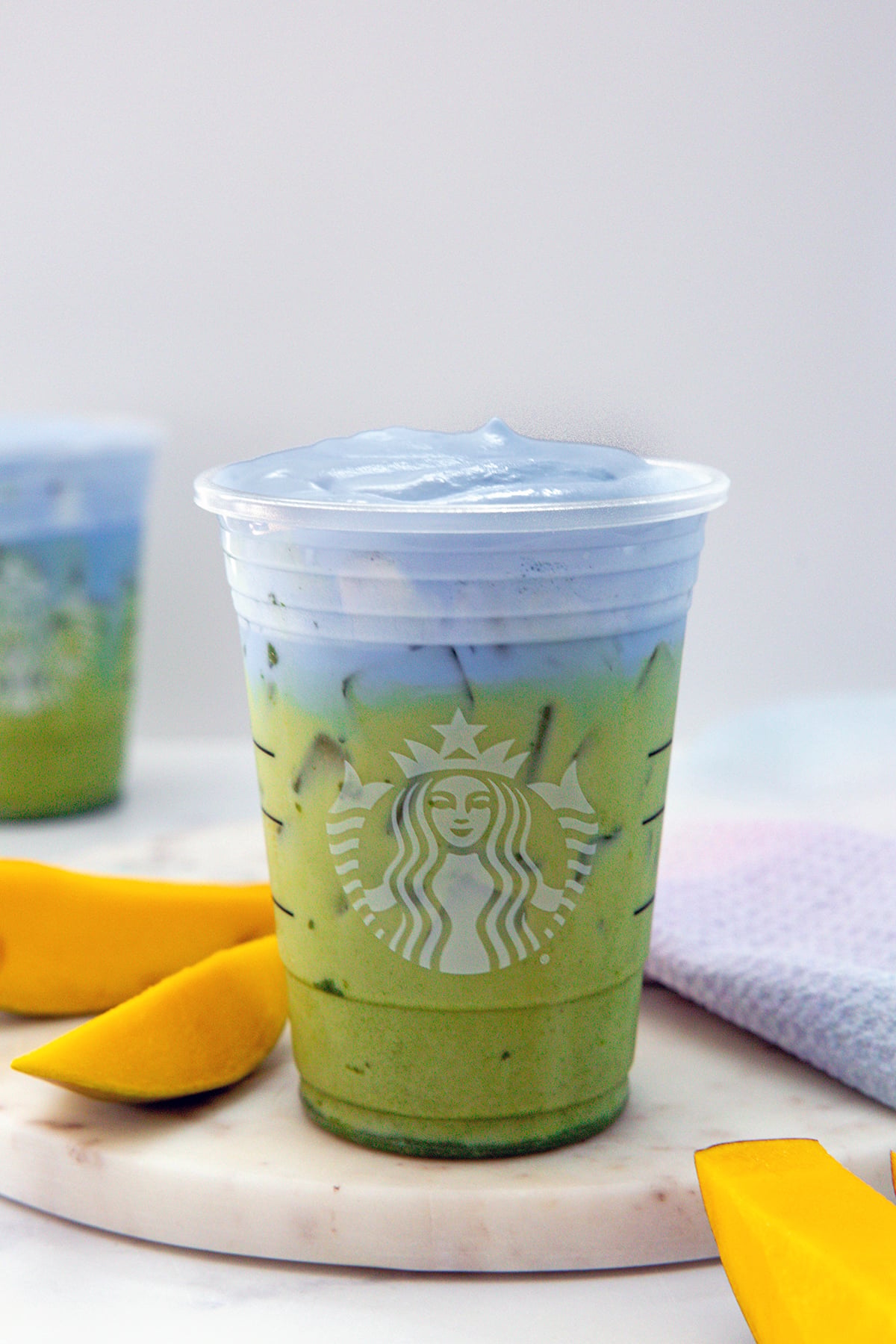 Head-on view of an iced Blue Coconut Matcha in a Starbucks cup with sliced mango all around.