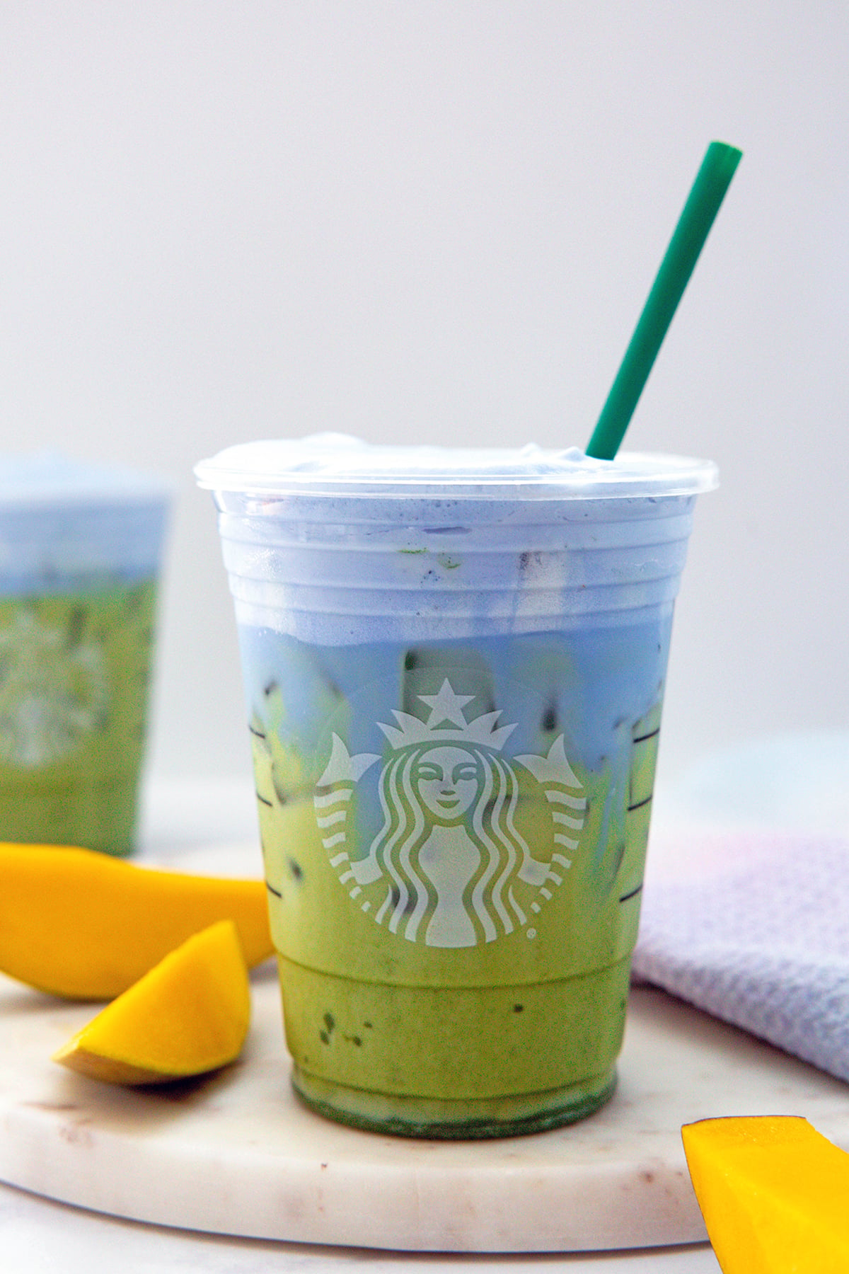 Head-on view of an iced matcha with blue coconut cold foam and sliced mango on the side.
