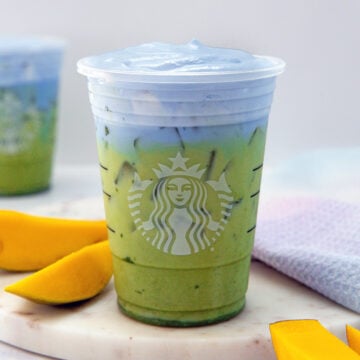 Closeup view of a homemade Starbucks Iced Blue Coconut Matcha with sliced mango in background.
