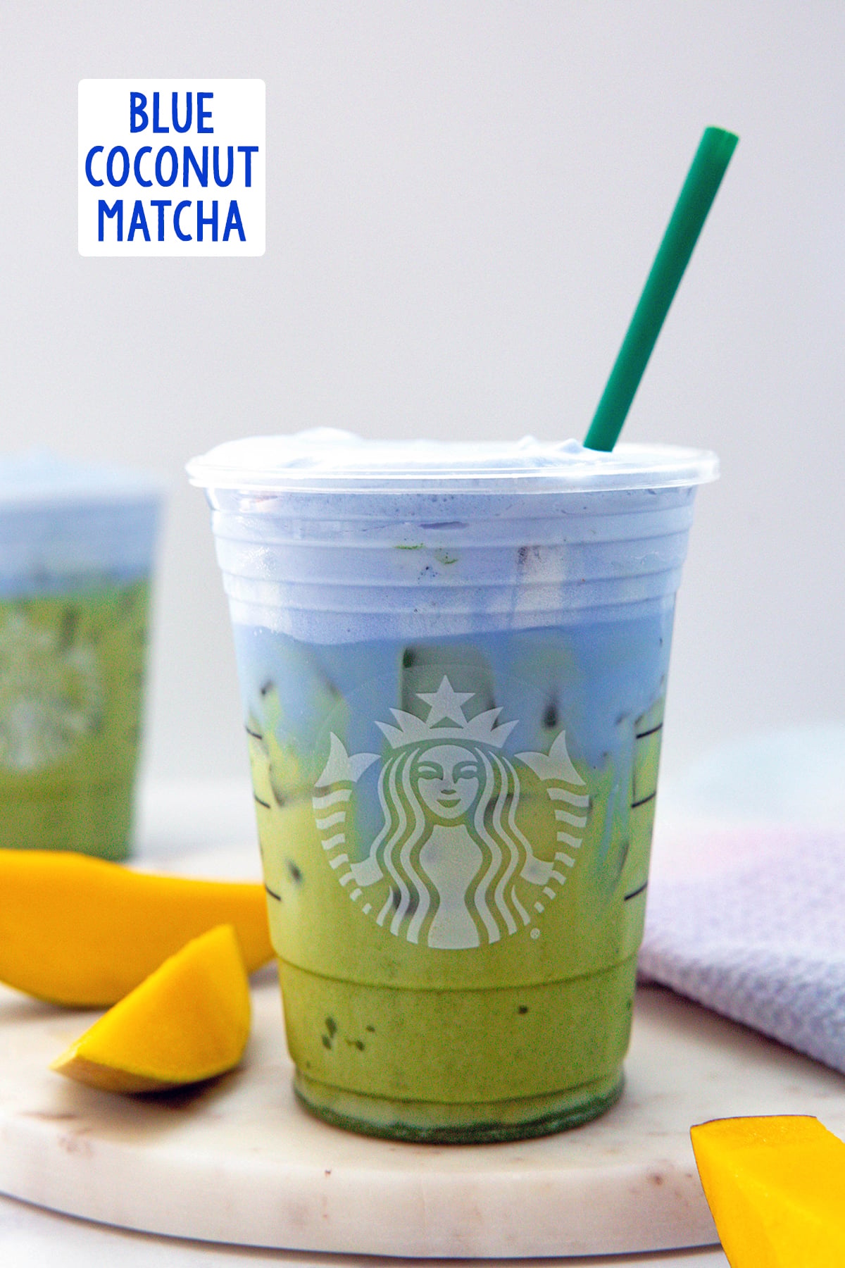 Head-on view of an iced matcha with blue coconut cold foam and sliced mango on the side with recipe title at top.