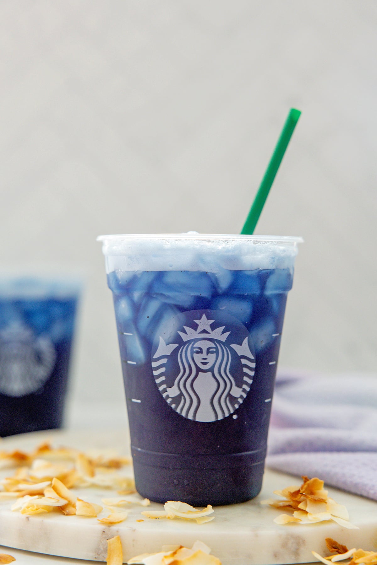 Head-on view of a Blue Coconut Refresher in a Starbucks cup with green straw and toasted coconut all around.