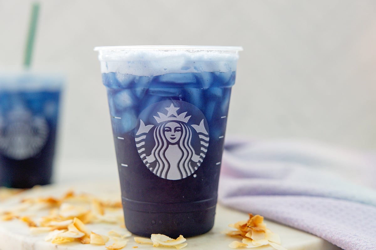 Head-on landscape view of a Blue Coconut Refresher with second drink in background and toasted coconut all around.