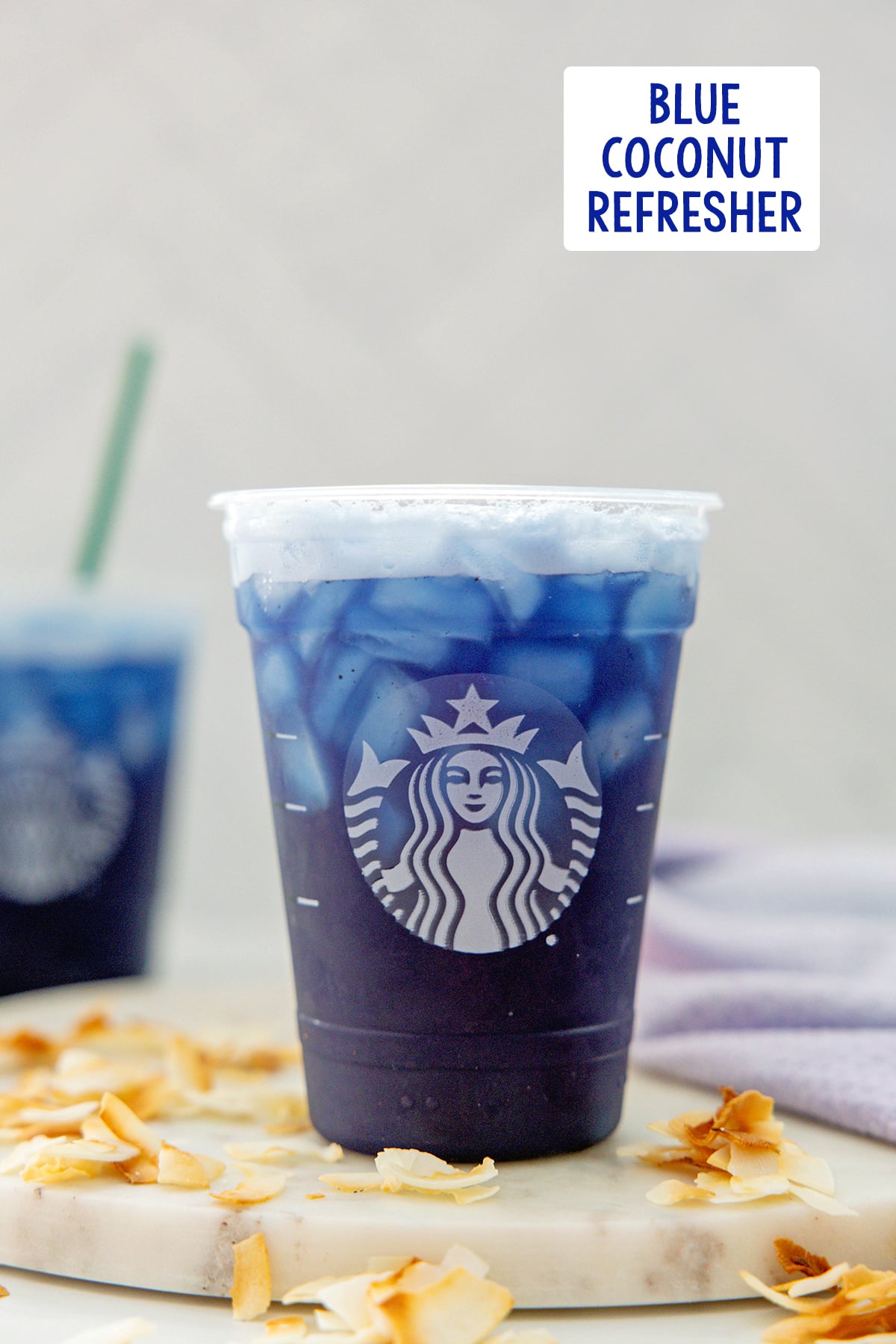 Head-on view of a Blue Coconut Refresher in a Starbucks cup with toasted coconut all around, second drink in background, and recipe title at top.