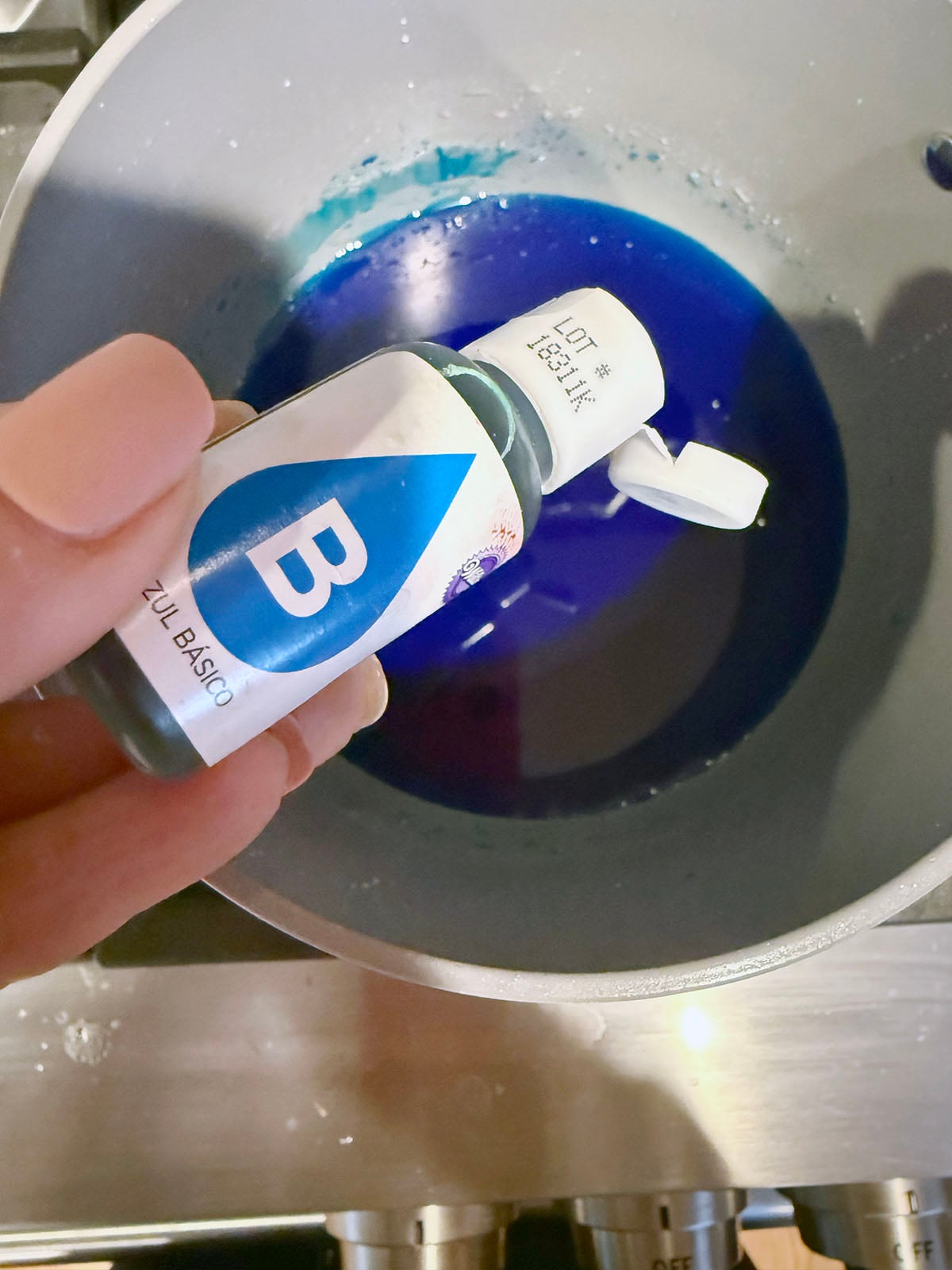 Blue food dye being dripped into syrup in saucepan.
