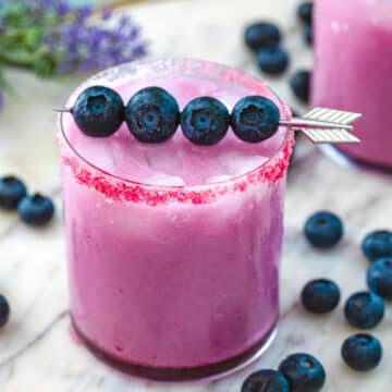 Closeup view of a blueberry coconut margarita with blueberry garnish and blueberries all around.