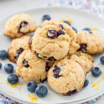 Blueberry, lemon, white chocolate chunk cookies on a plate with fresh blueberries and lemon zest all around.