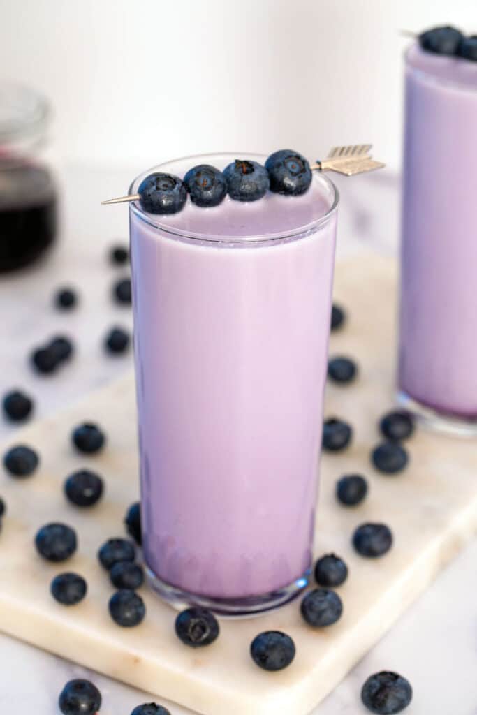 Overhead view of a glass of blueberry milk with fresh blueberry garnish, second glass in background, and blueberries all around.