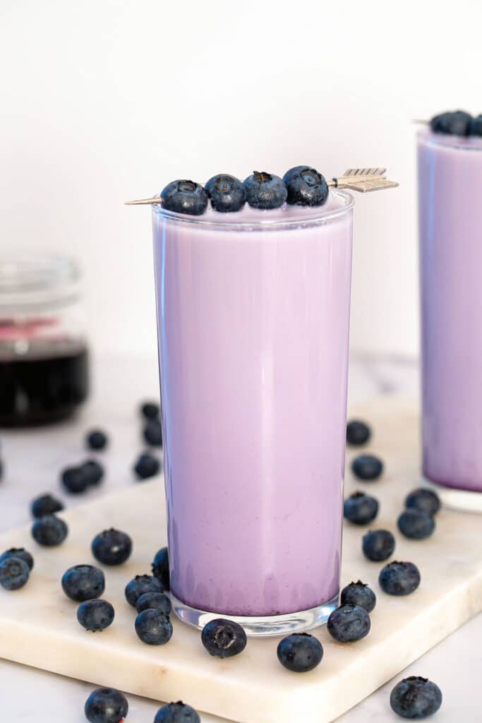 Head-on view of a glass of blueberry milk with blueberries all around and on garnish.