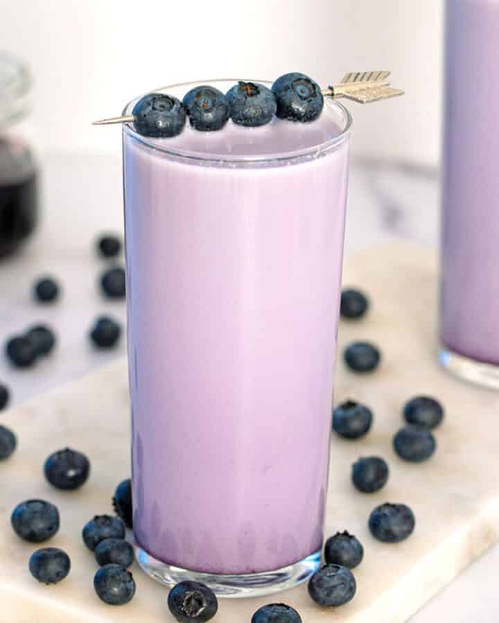 Close-up of a glass of blueberry milk with fresh blueberry garnish with blueberries all around.