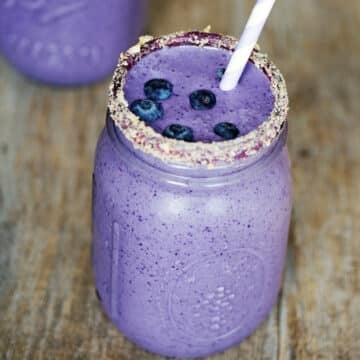 Purple blueberry ie milkshake in a mason jar with graham cracker crumb rim and fresh blueberries.