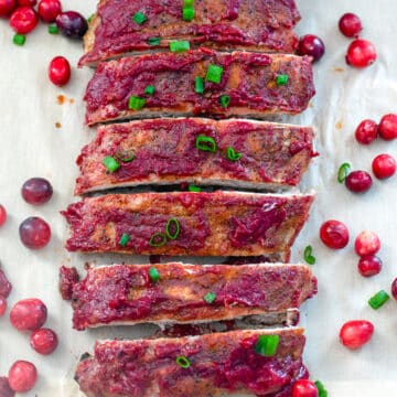 Closeup view of bourbon cranberry ribs with fresh cranberries and scallions all around.