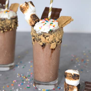 Closeup view of a bourbon s'mores milkshake with graham cracker rim and marshmallow, sprinkles, and chocolate bar toppings.