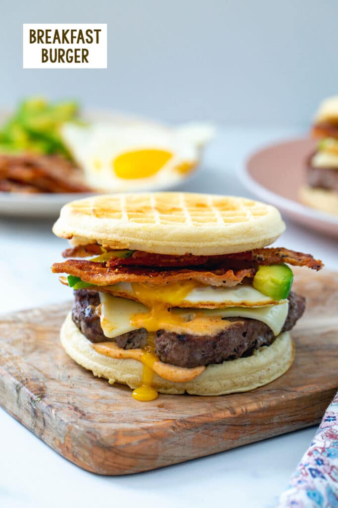 Breakfast burger on waffles with egg, bacon, cheese, avocado, and sauce with recipe title at top.