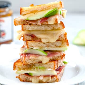 Closeup view of a stack of brie grilled cheese sandwich halves with green apple, prosciutto, and fig spread.