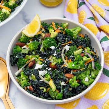 Closeup view of a broccoli kale salad with lemon wedge in bowl.