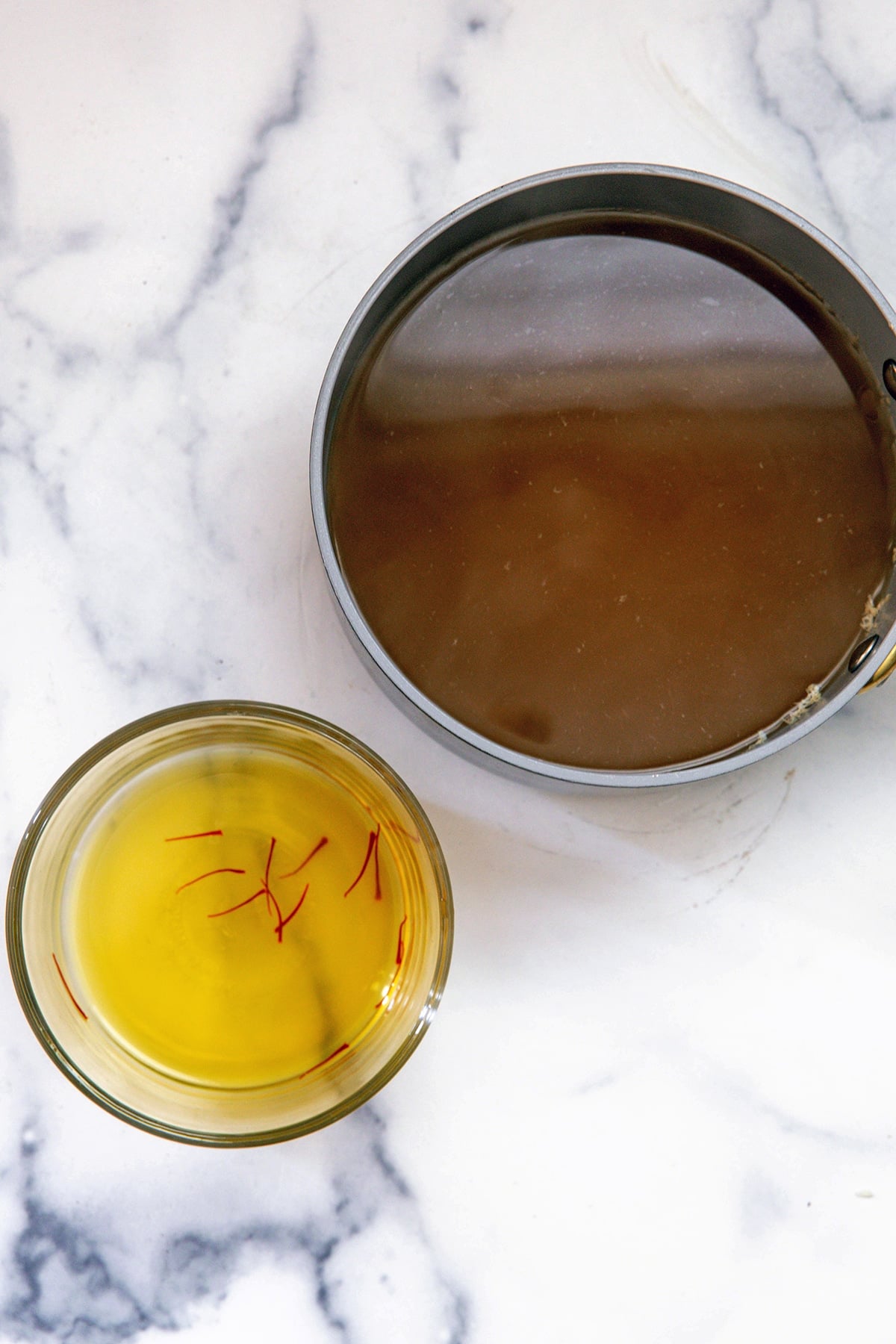 Broth in saucepan and saffron broth in small bowl.
