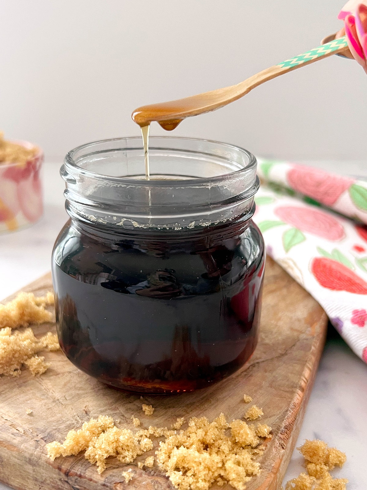 Small jar of brown sugar syrup with spoon held over dripping syrup off of it.