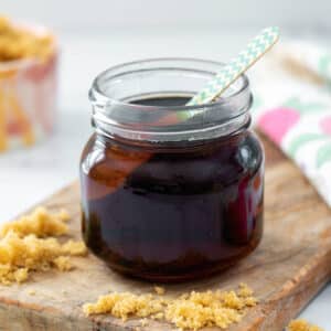 Closeup view of a small jar of brown sugar syrup with spoon with light brown sugar sprinkled around.