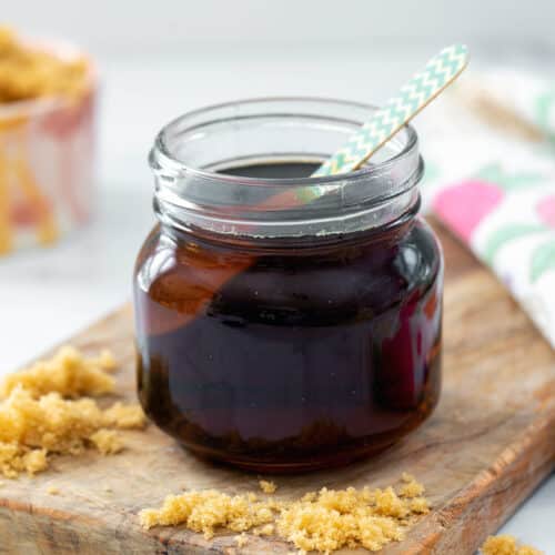 Closeup view of a small jar of brown sugar syrup with spoon with light brown sugar sprinkled around.