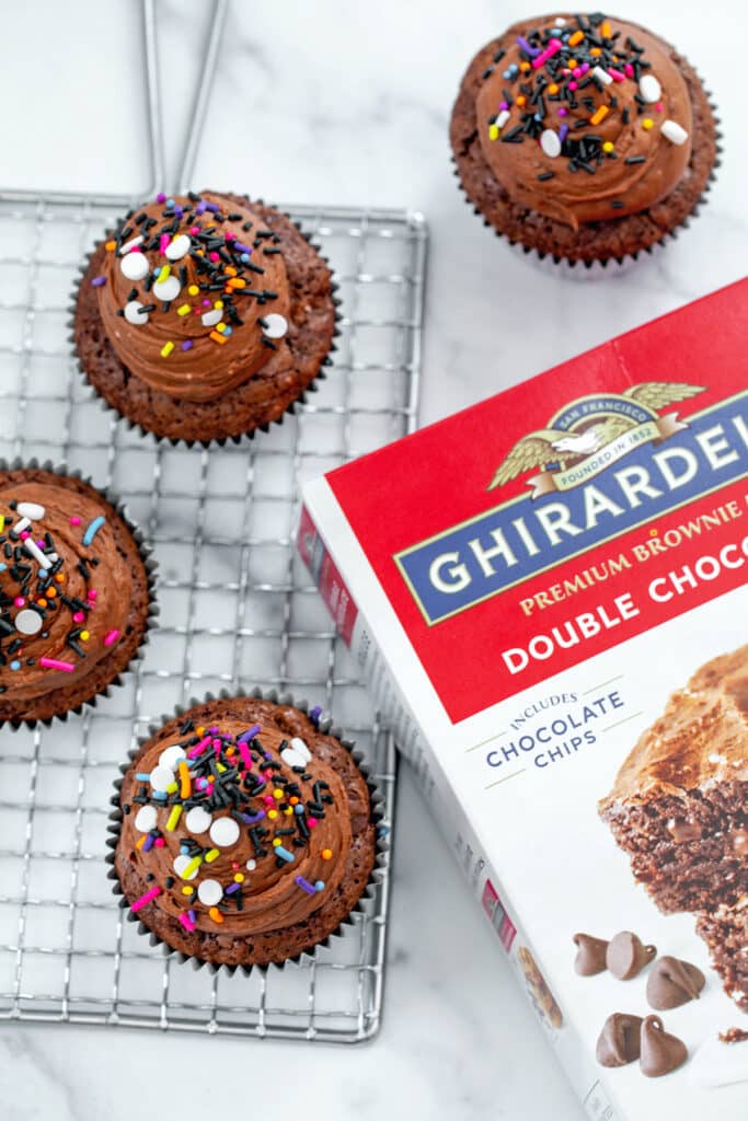 Overhead view of brownie mix cupcakes on metal rack with box of Ghirardelli brownie mix.